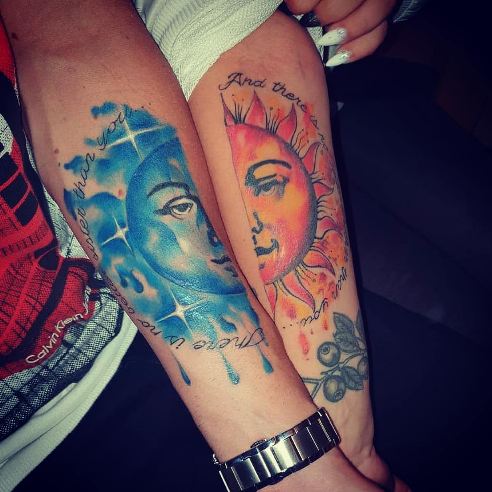 Arm tattoos of blue moon and orange sun with matching scripts on two inner forearms